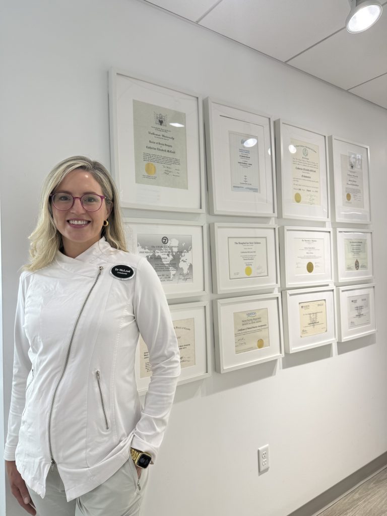 Dr. Catherine McLeod beside her framed degrees and certifications at Embrace Orthodontics, Halifax